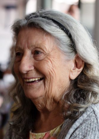 An elderly woman with gray hair is looking into the distance and smiling.