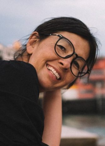 A woman with dark hair and glasses sits and smiles at the camera.